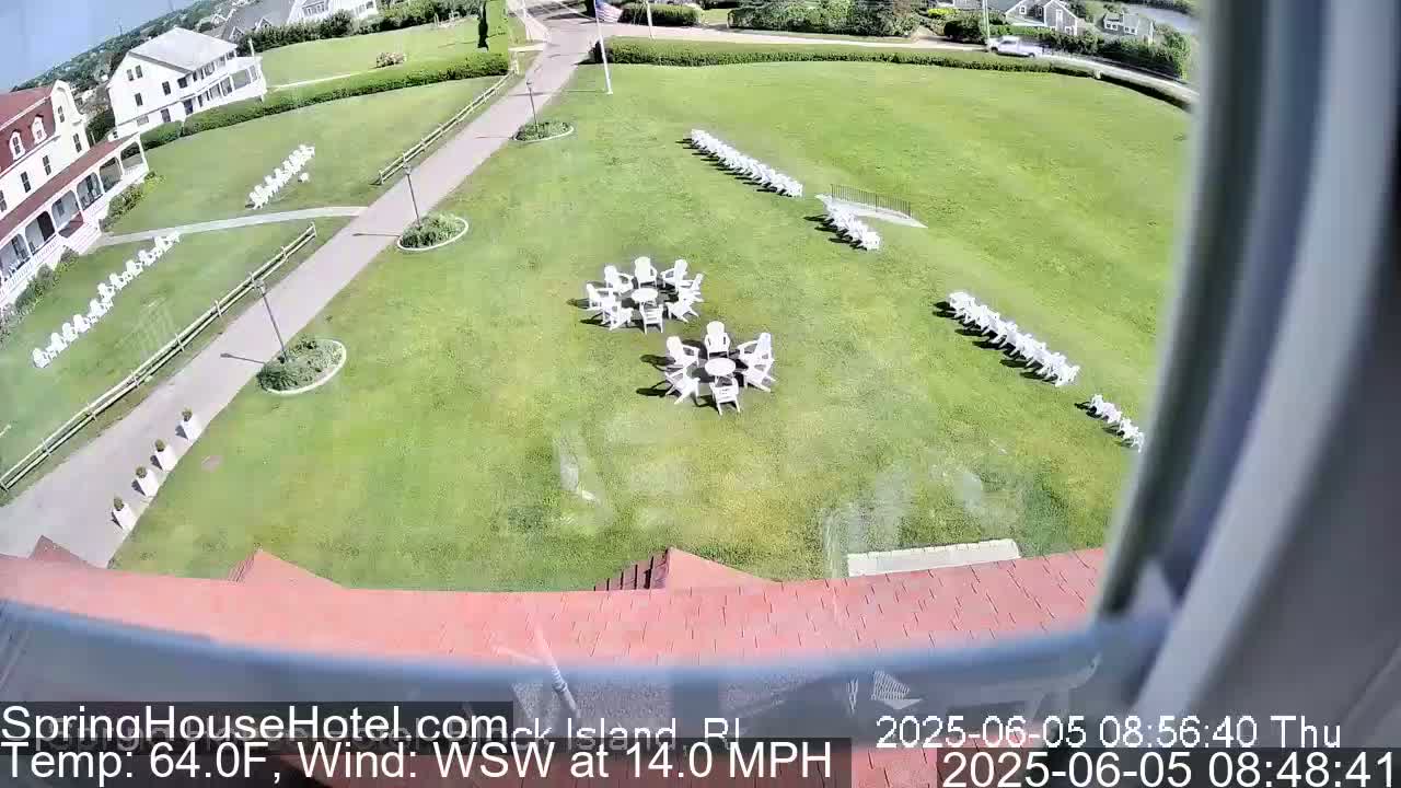 A high-angle view shows a grassy lawn with numerous white chairs arranged in groups and lines, near a building on a sunny day with a WSW wind at 14.0 mph.