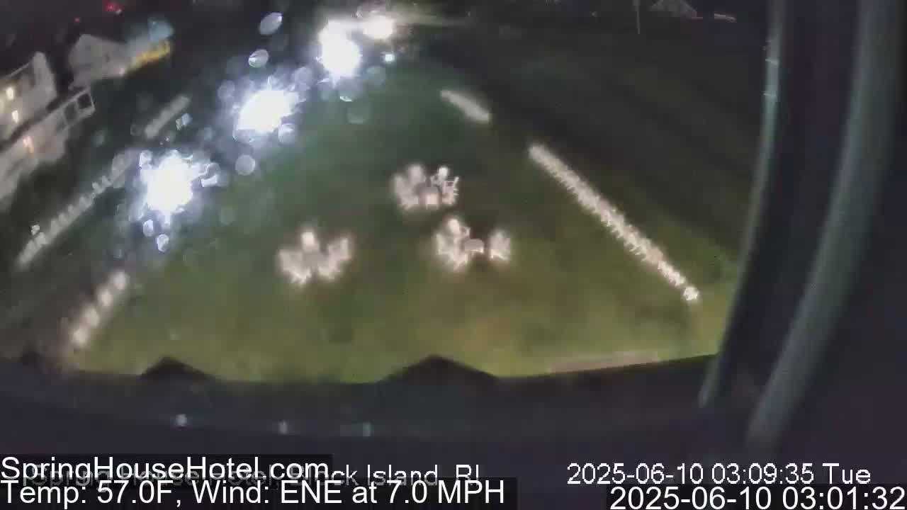 A nighttime, blurry outdoor view shows numerous small, indistinct objects scattered across a grassy area, with a 7 mph wind from the east-northeast and a temperature of 57°F.