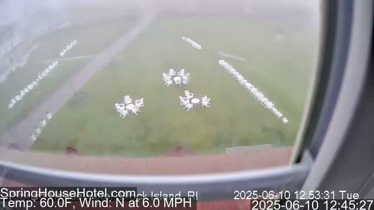 A foggy view from a window shows a grassy area with several sets of white patio furniture arranged in groups and long rows.