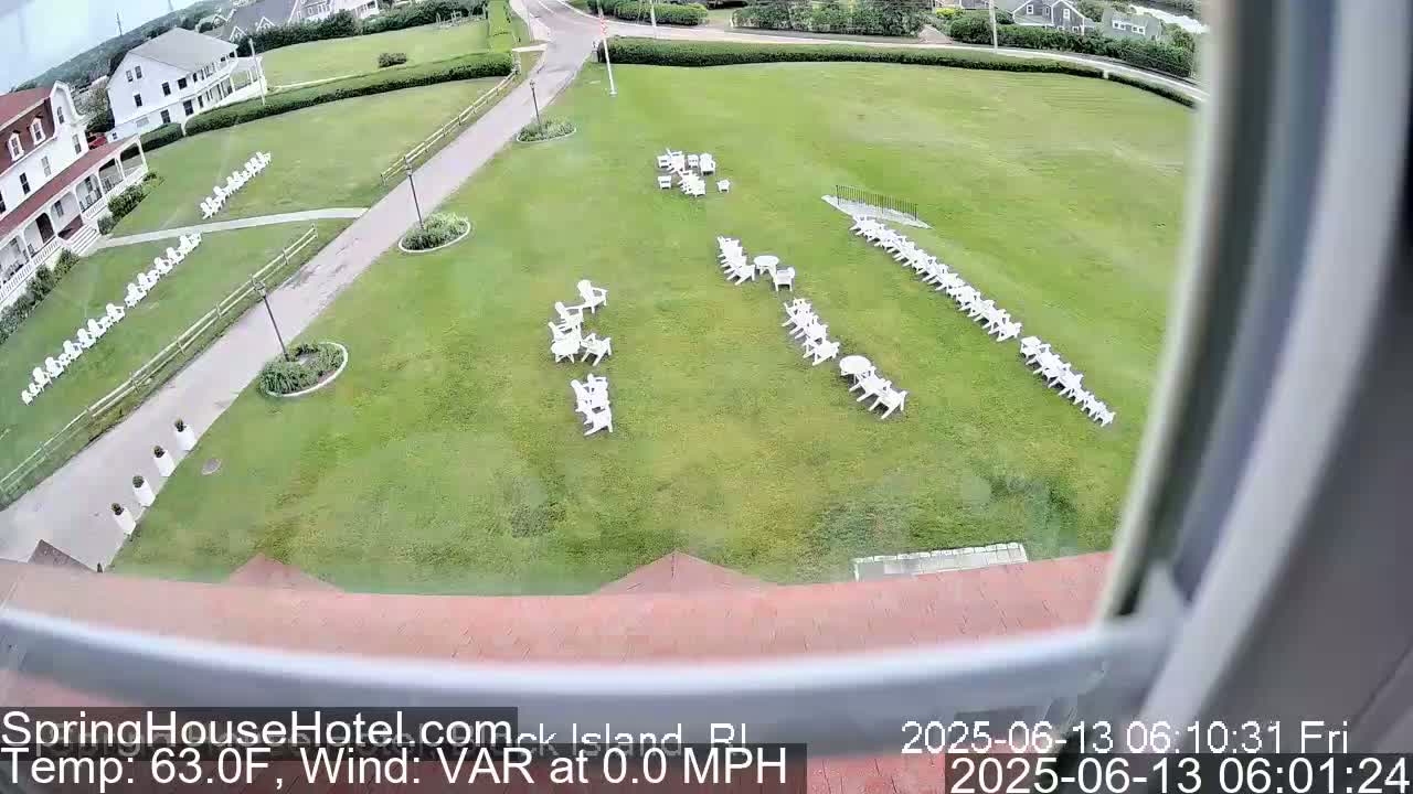 A large grassy area with numerous white chairs arranged in rows and small groupings, viewed from a window on a partly cloudy day.