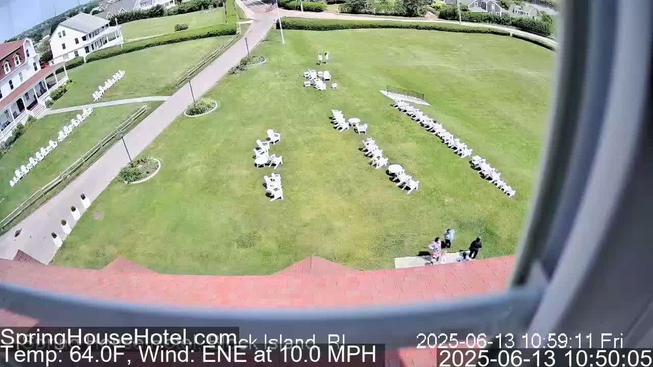 An elevated view shows a grassy area with rows of white chairs and tables, a building, and several people walking on a pathway, all under sunny conditions with a 10 mph east-northeast wind.