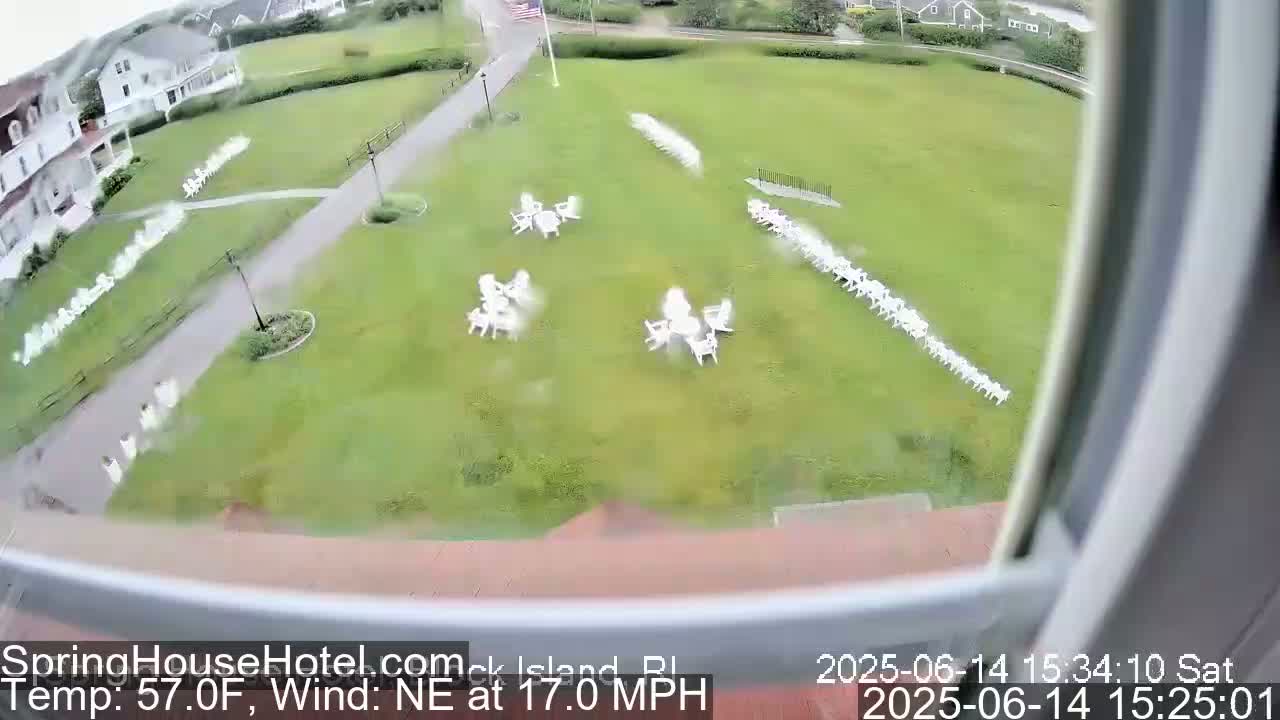 A white van is driving on a paved path next to a grassy area with numerous white lawn chairs and small tables arranged in groups, under an overcast sky with a 16 mph east wind and a temperature of 60°F.