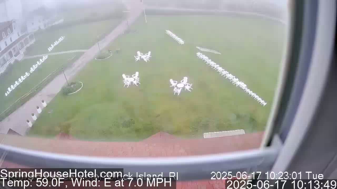 A grassy area with numerous white chairs and small tables is visible through a window on a foggy day with an easterly wind blowing at 7.0 mph and a temperature of 59.0°F.