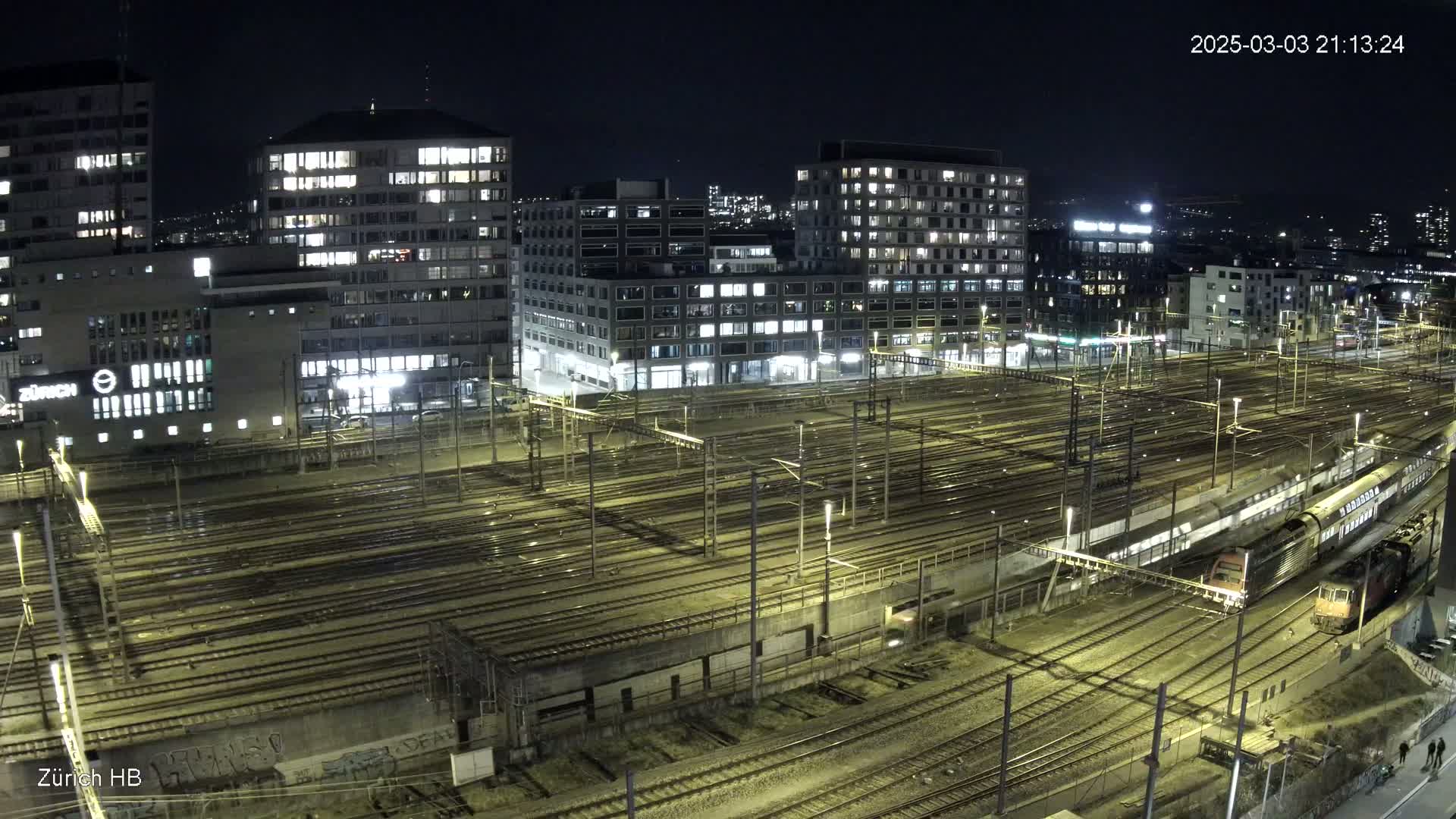 A nighttime, high-angle view of a large train yard surrounded by illuminated buildings.