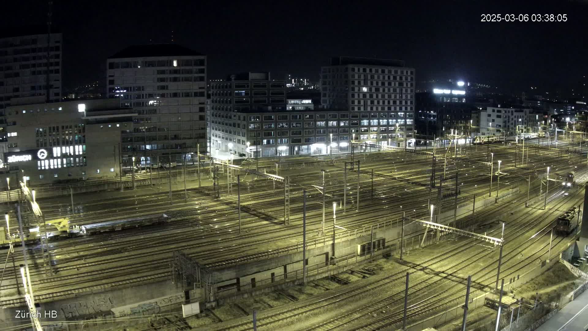 A nighttime, high-angle view of a large train yard surrounded by illuminated buildings.