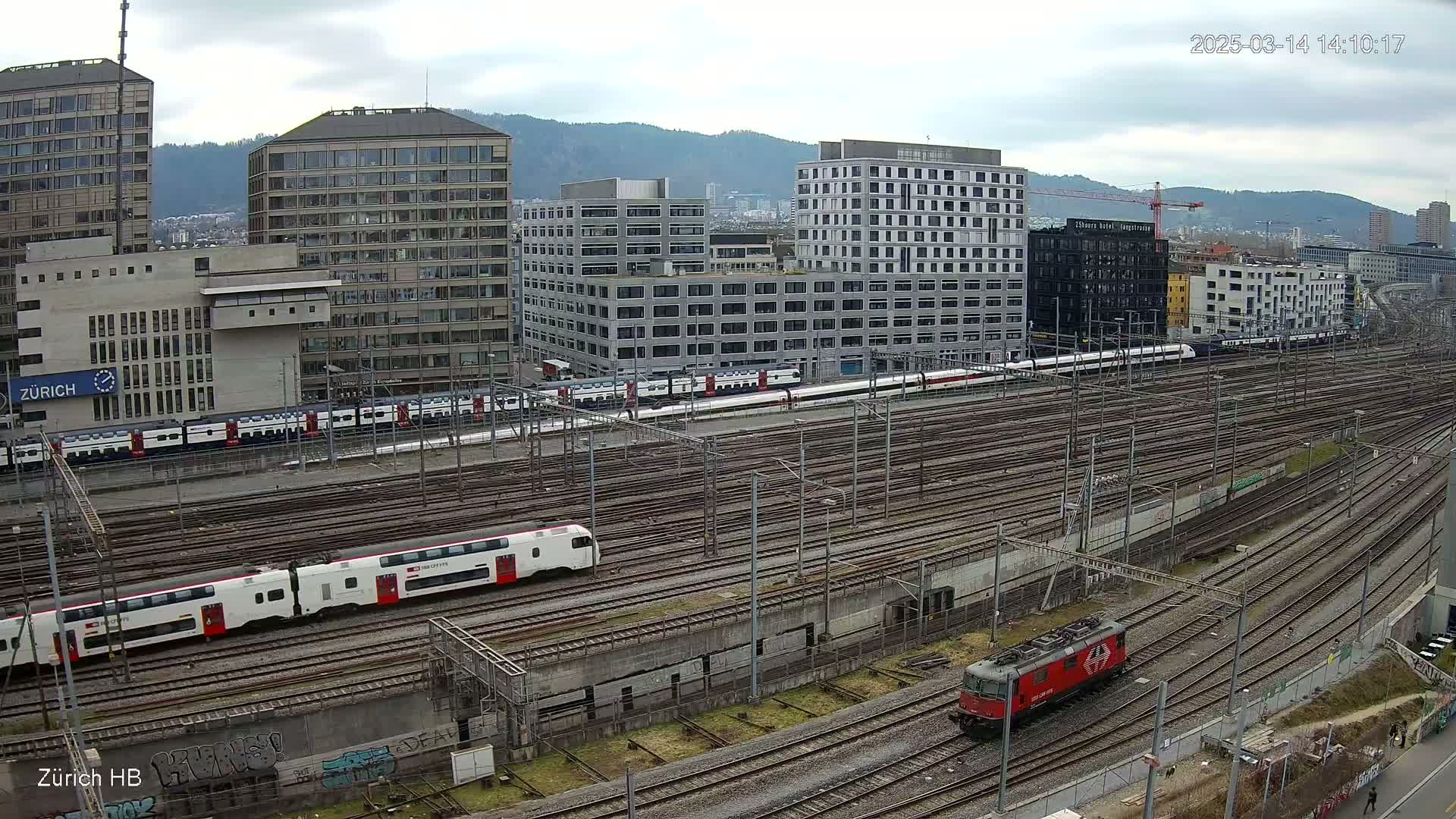 A high-angle view of a railway yard with multiple trains and modern buildings under an overcast sky.