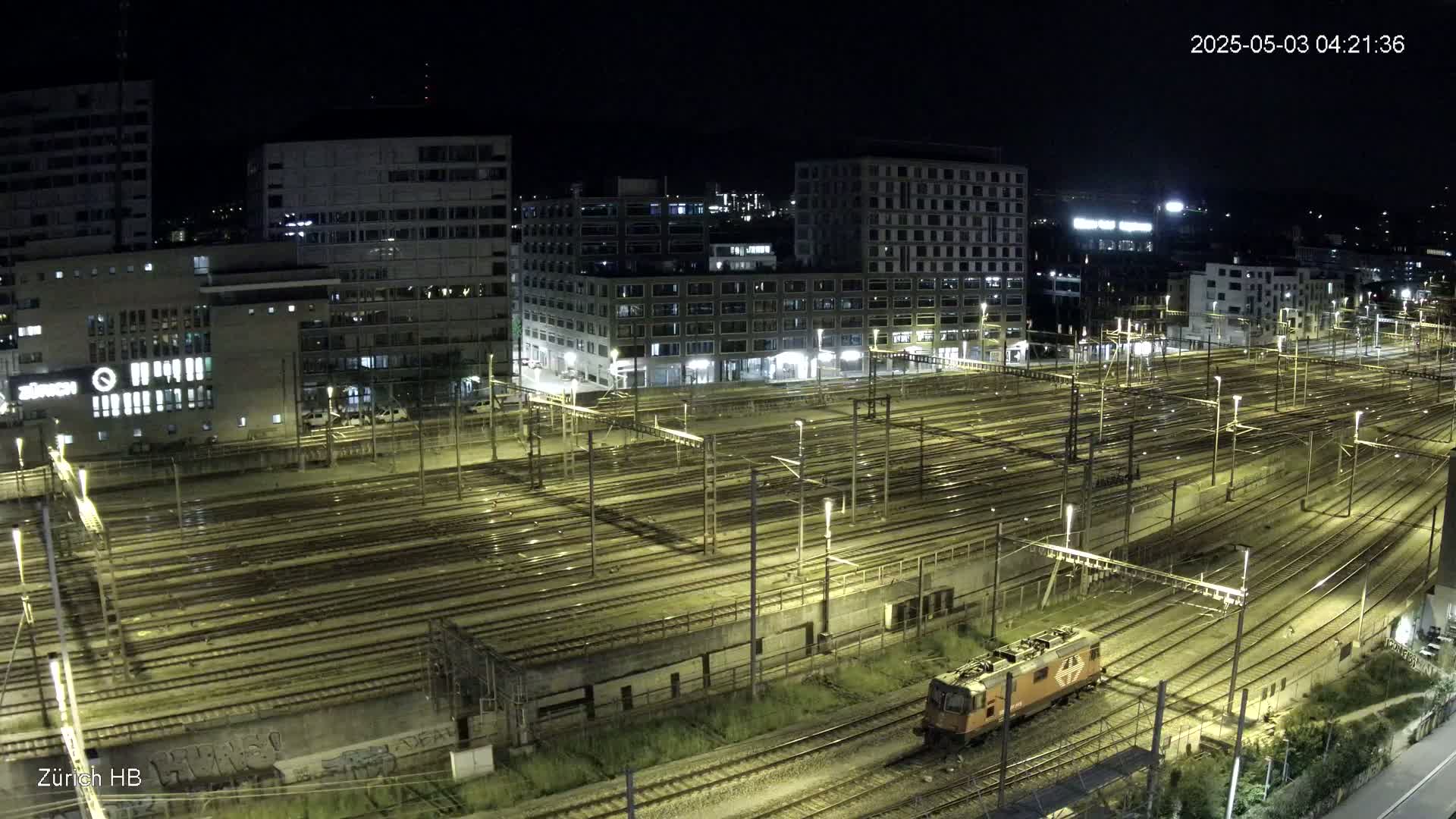 A nighttime aerial view of a large train yard with many tracks and buildings surrounding it.