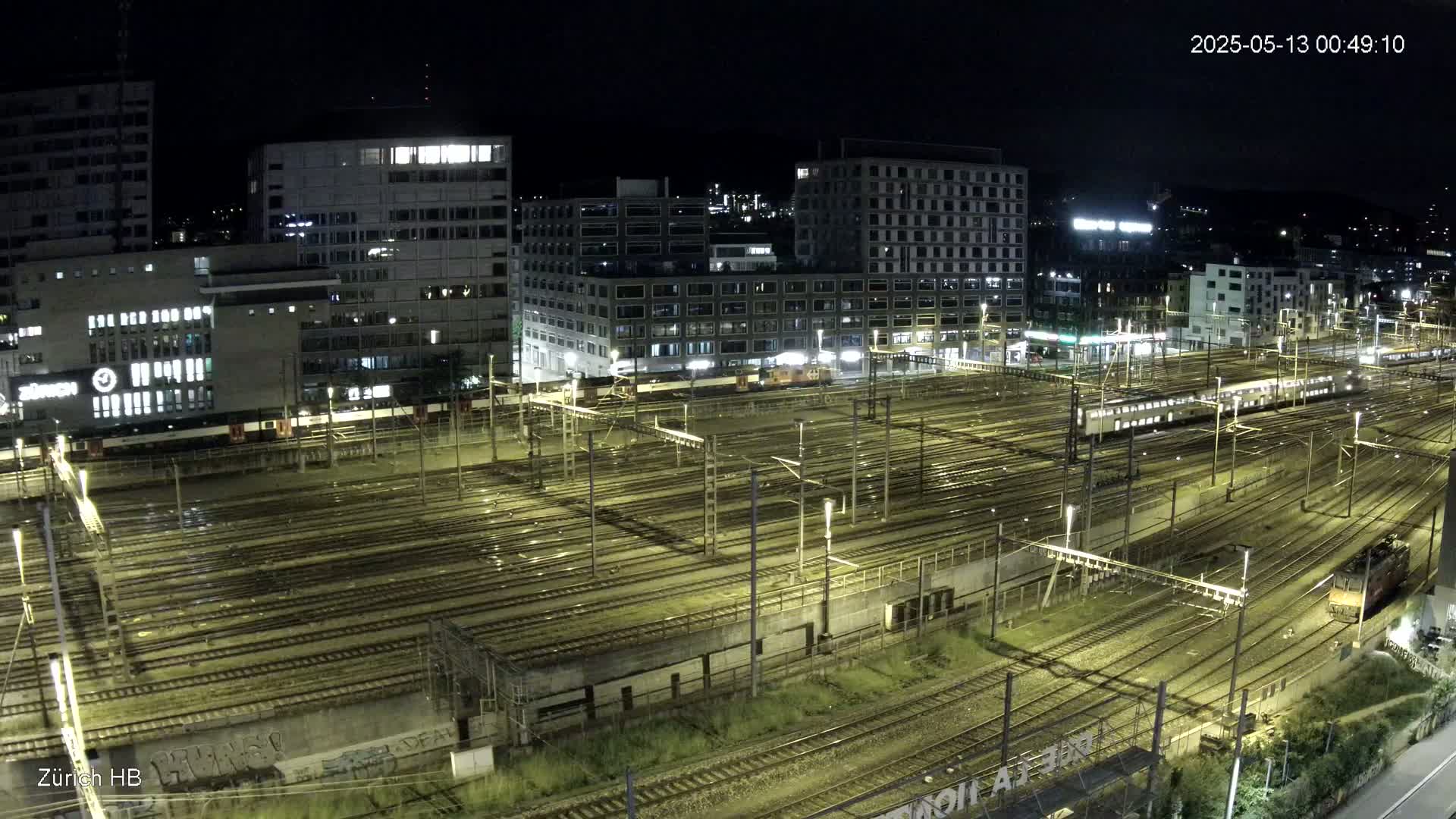 A nighttime, wet view of a large train yard surrounded by city buildings.