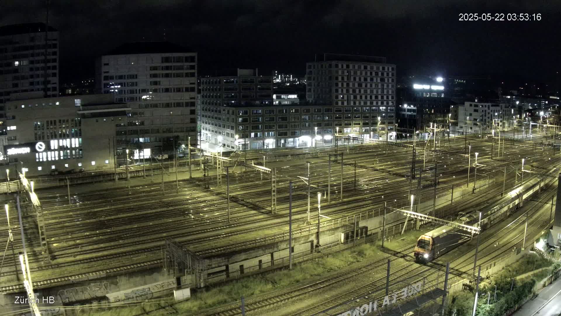 A nighttime view of a train station with many tracks and buildings surrounding it, under a clear sky.
