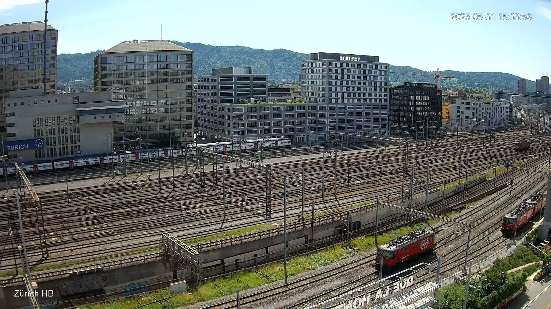 A sunny day overlooking a large train yard with many tracks and several modern buildings in the background.