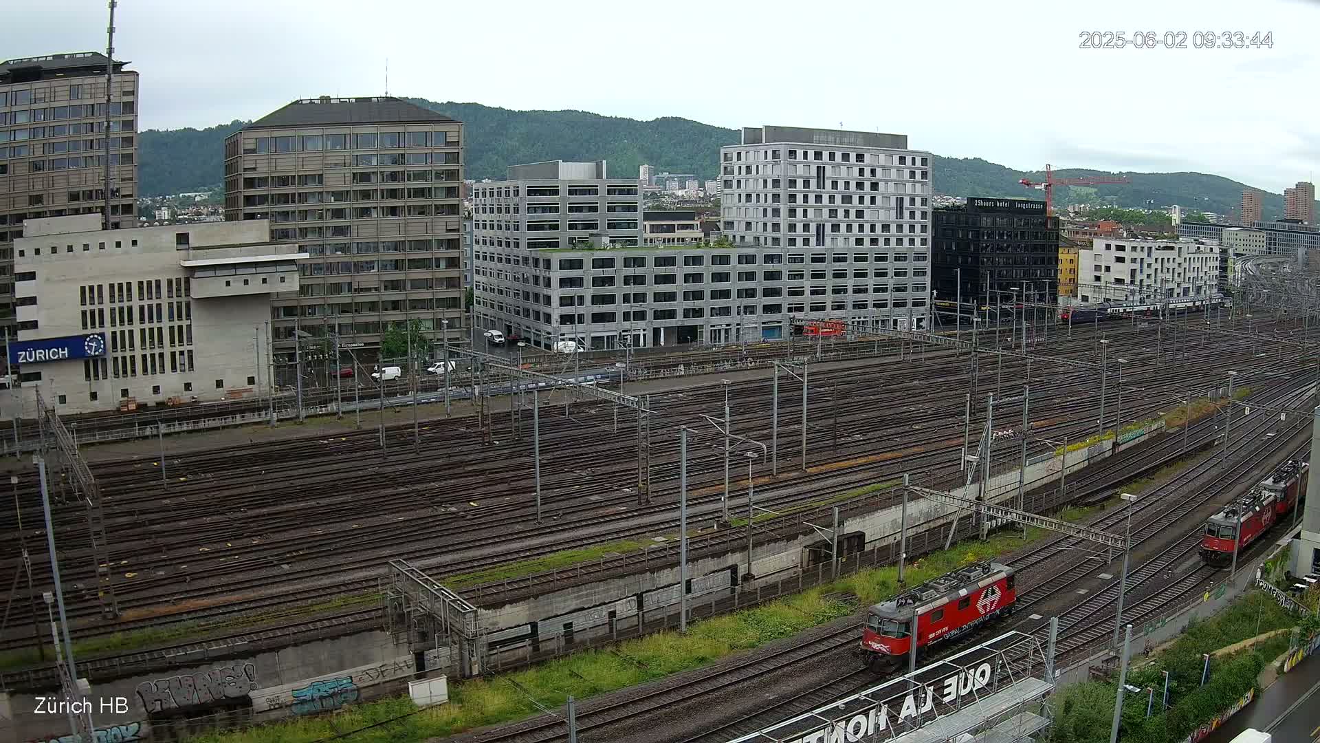 A sprawling network of train tracks in a city, surrounded by modern buildings under an overcast sky.