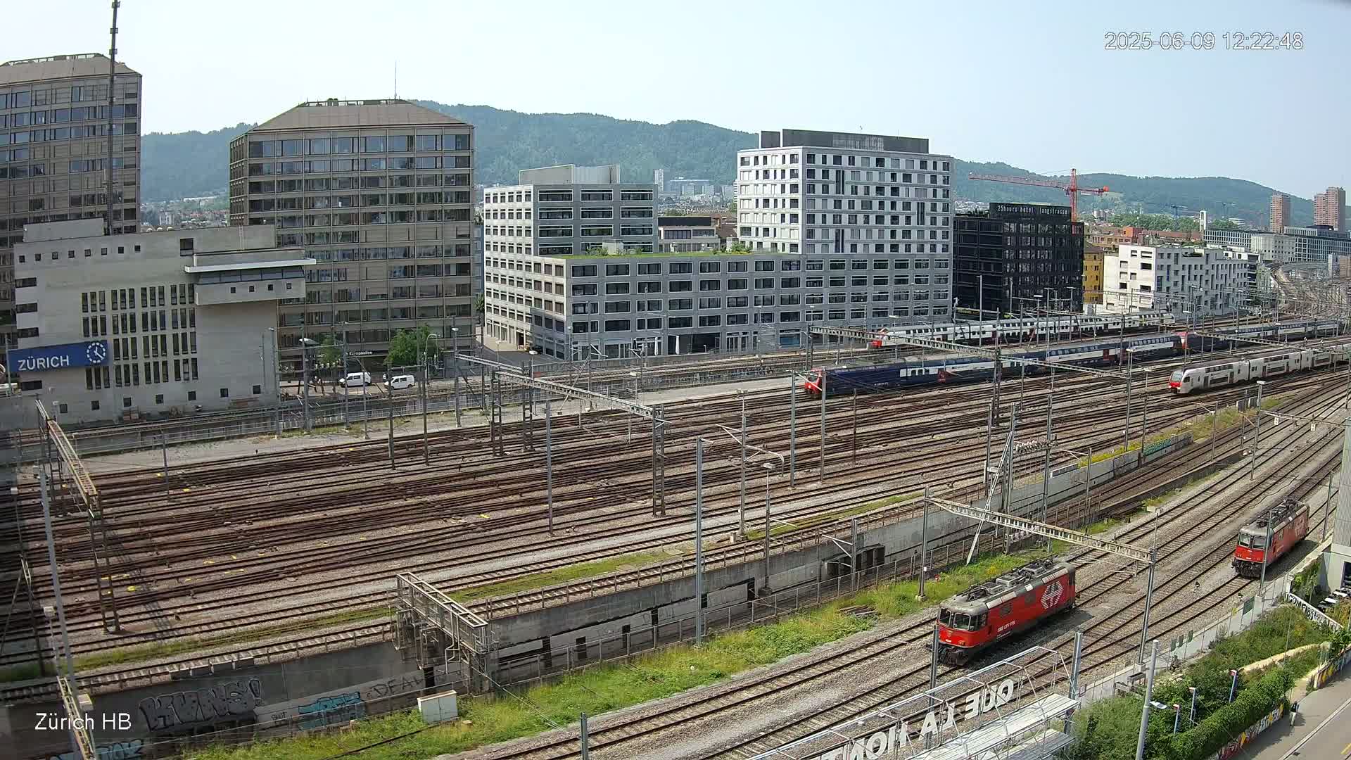 A sunny day view of a large railway yard with multiple trains and modern buildings in the background.