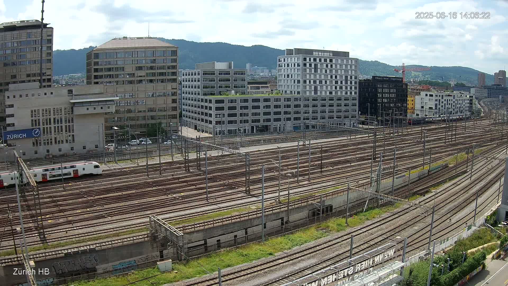 A sprawling railway yard with numerous tracks, surrounded by modern buildings under a partly cloudy sky.