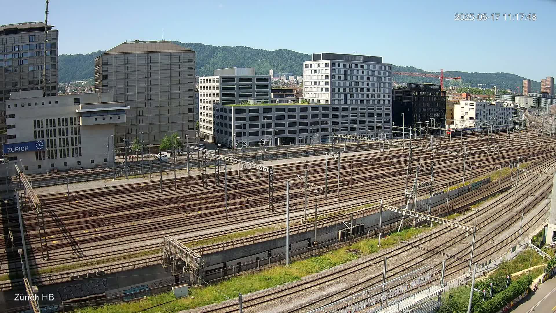 A large expanse of train tracks stretches out before numerous buildings under a clear, sunny sky.