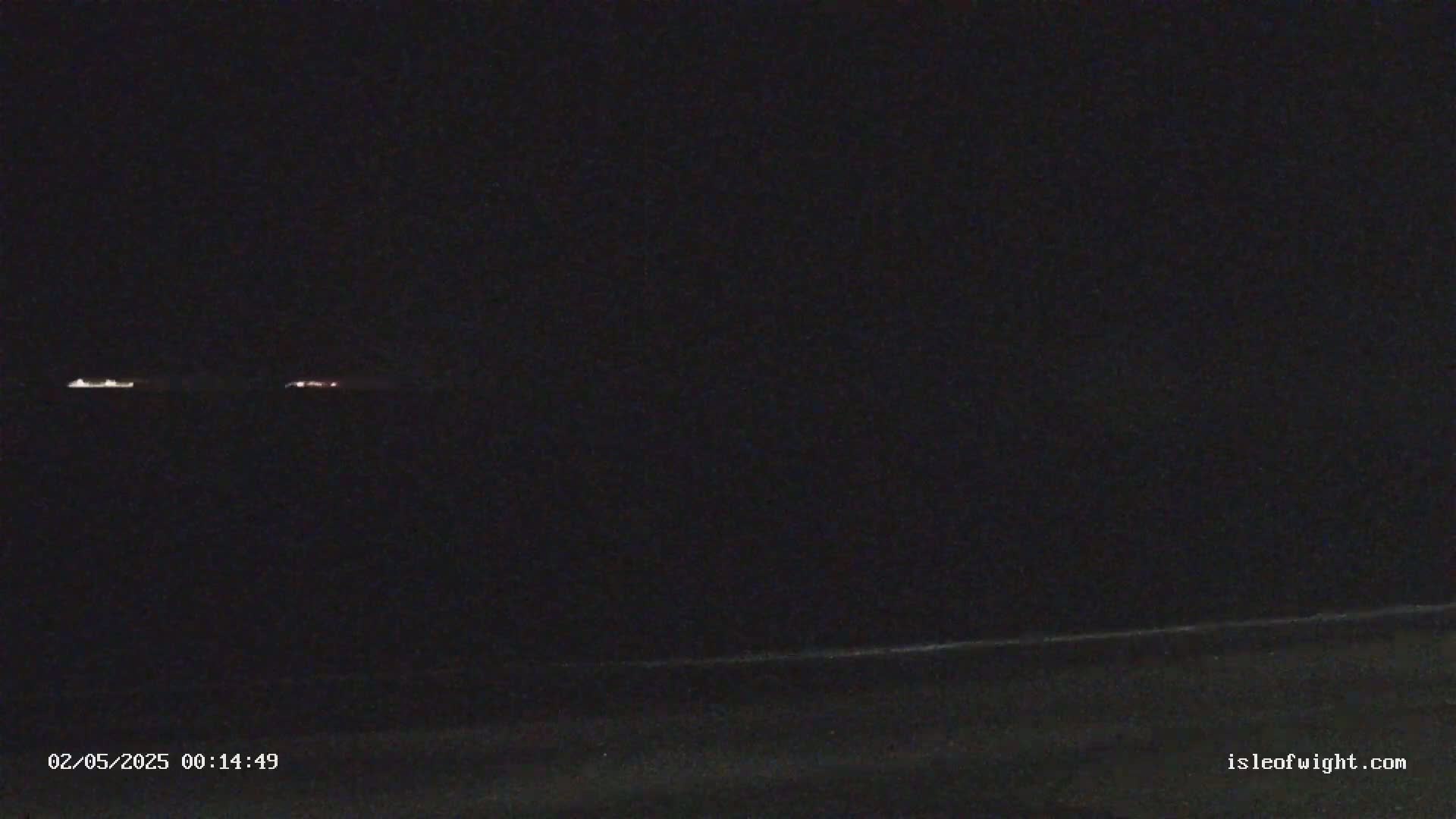 At night, faint lights are visible on the horizon over a dark body of water.