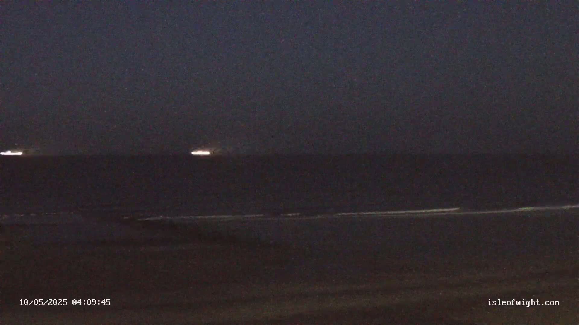 A dark, nighttime coastal scene shows a calm sea with faint lights on the horizon.