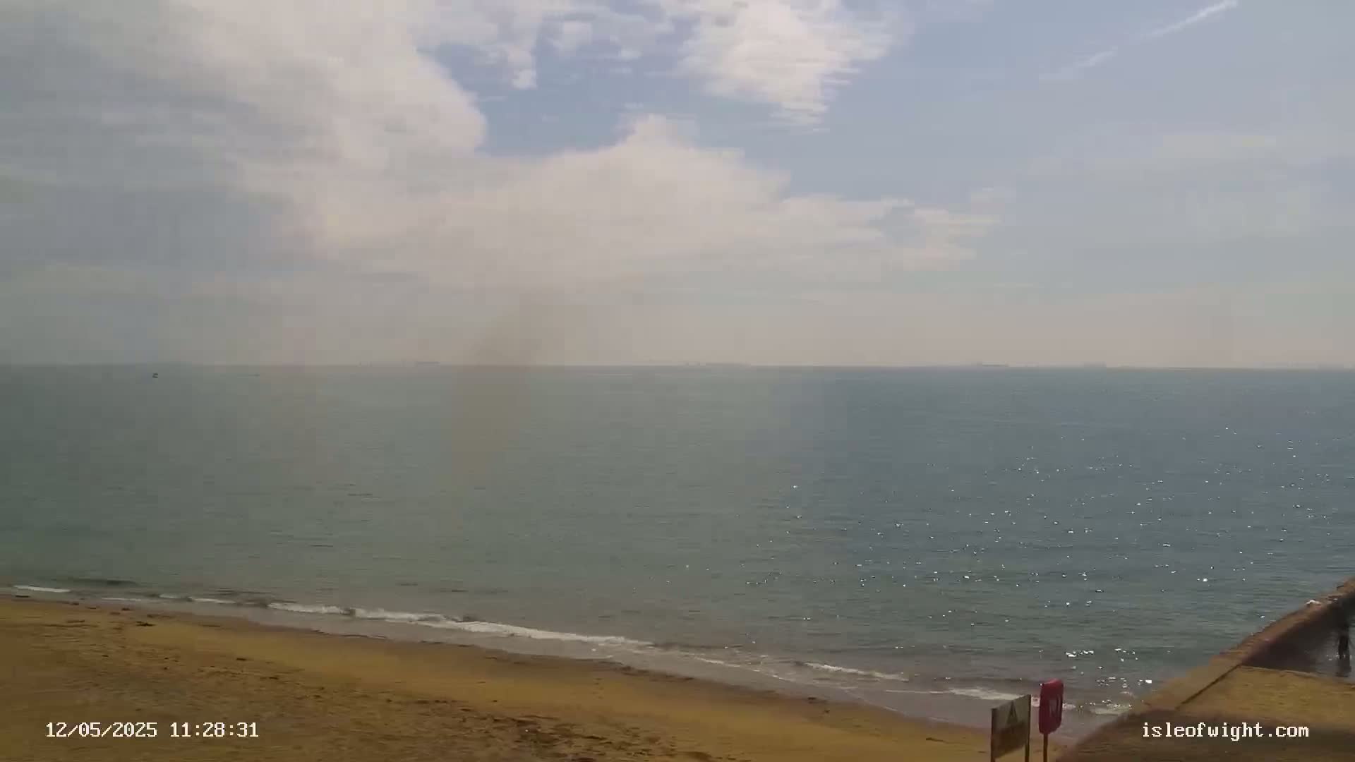 A sandy beach meets a calm, somewhat hazy sea under a partly cloudy sky.