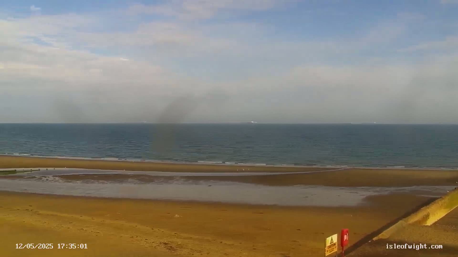 A wide sandy beach stretches towards a calm sea under a partly cloudy sky.