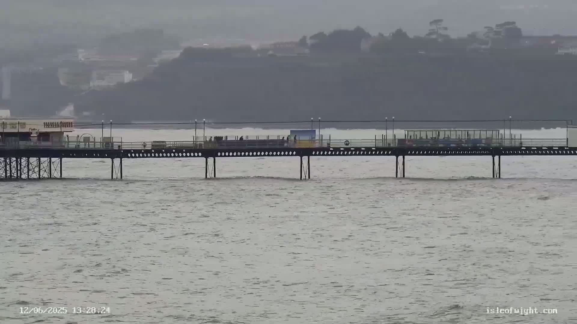 A pier extends over a choppy sea under an overcast sky.
