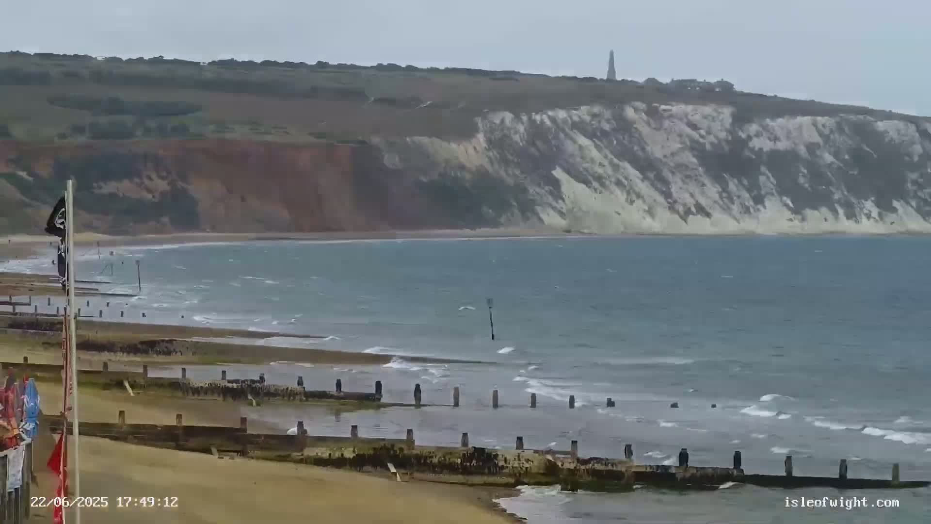 A sandy beach with a calm sea and a tall, white cliff in the background on an overcast day.