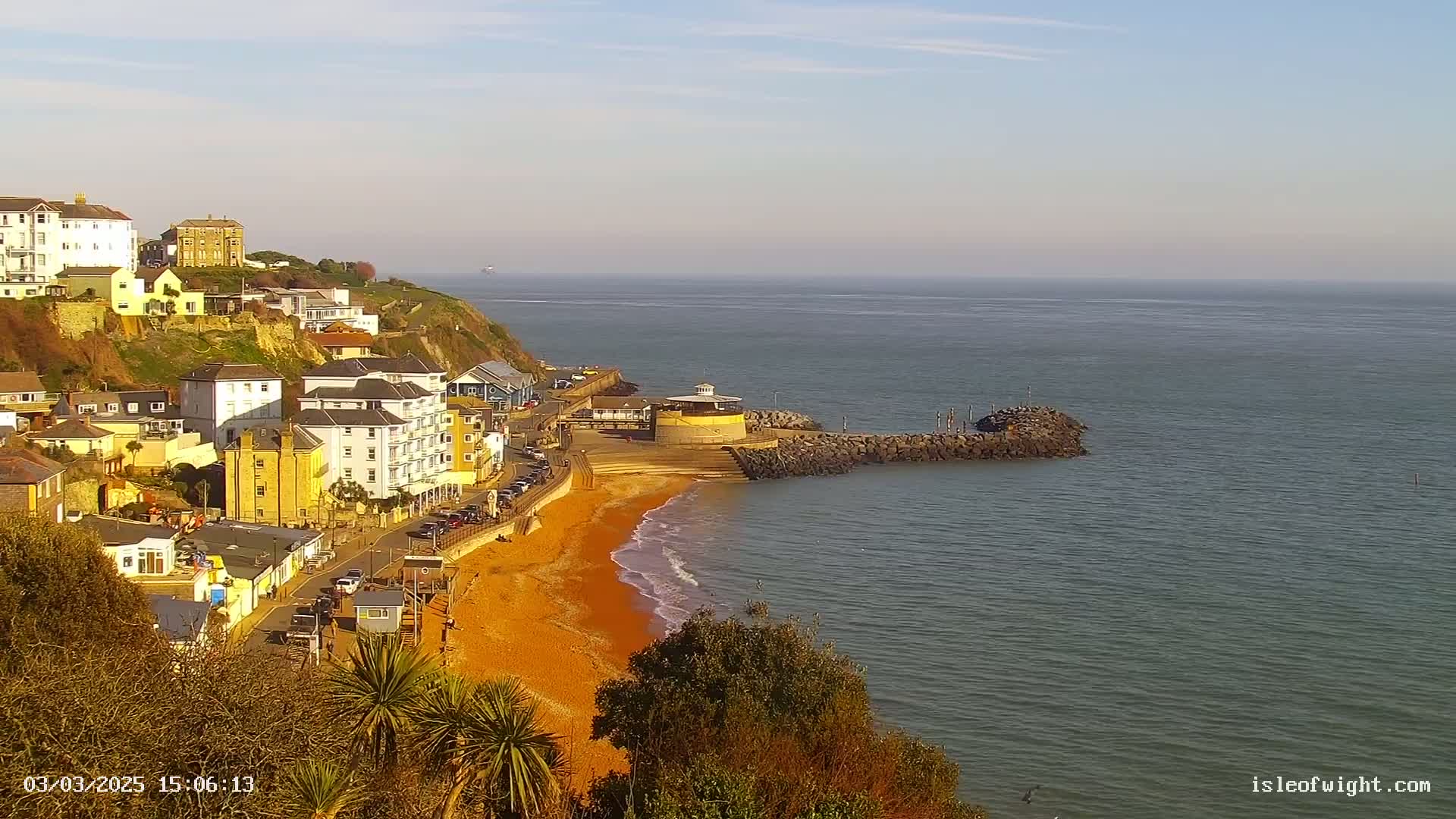 A coastal town overlooks a calm, ocean with a sandy beach, under a clear, sunny sky.