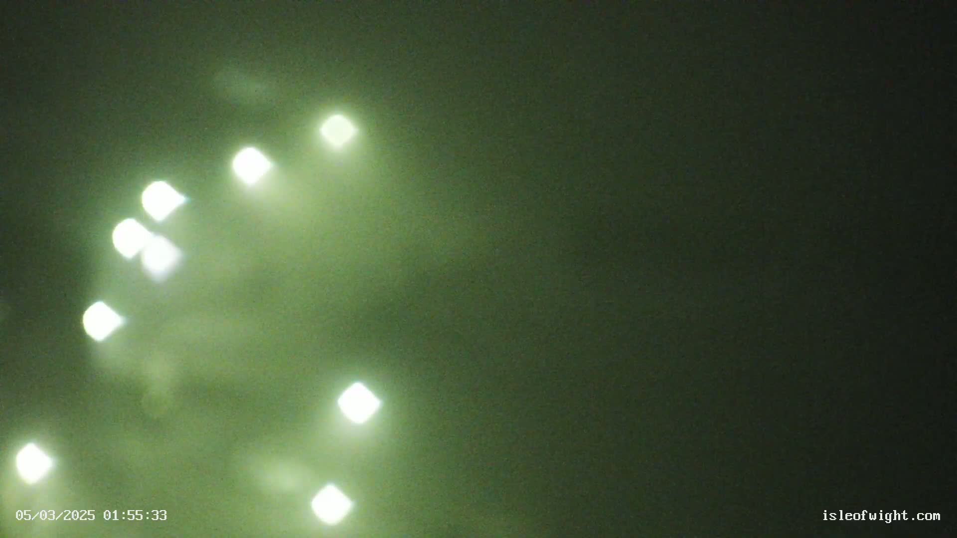 A blurry image shows several bright lights in a dark, foggy green-tinged night sky.
