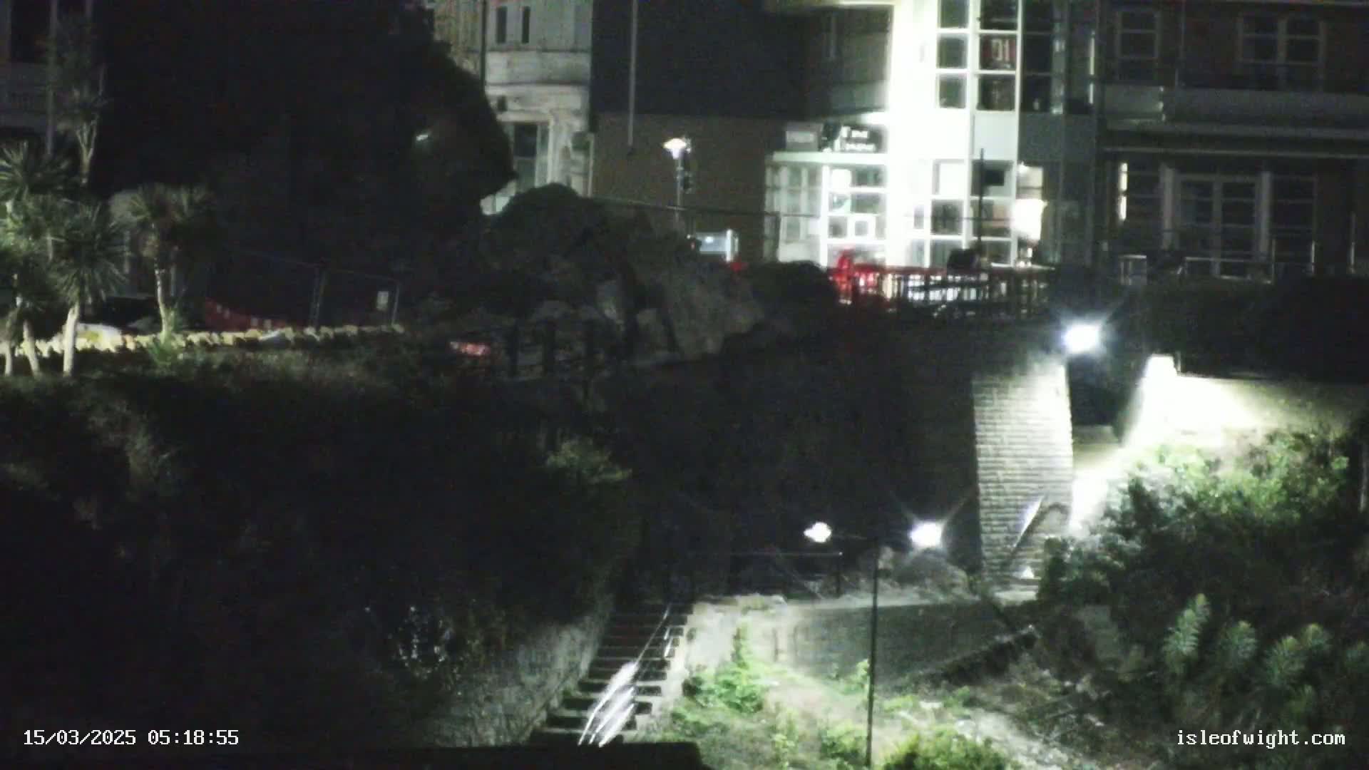 Nighttime view of a stone staircase leading down from a brightly lit building to a dark, vegetated area below.