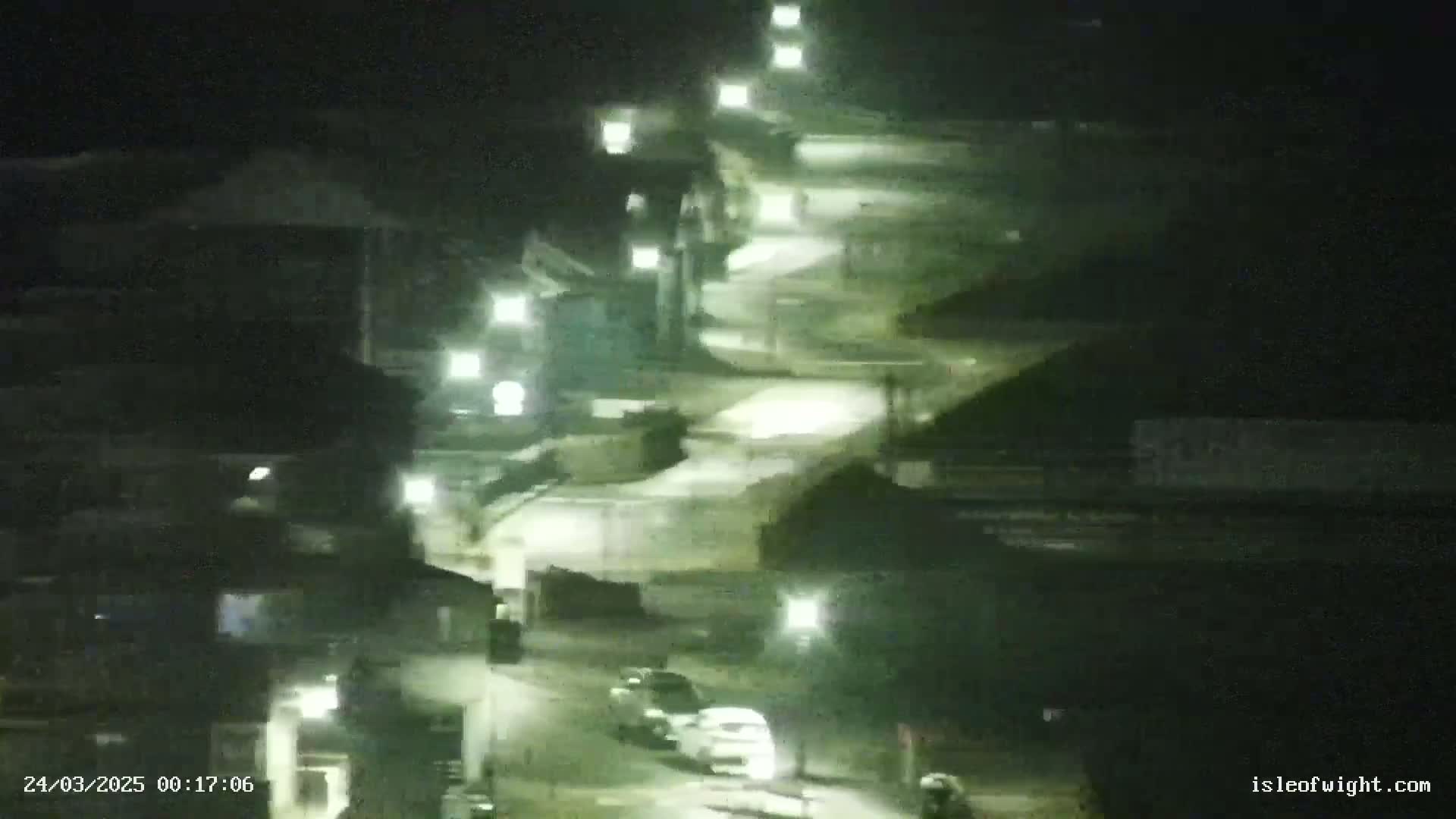 A nighttime view of a winding road illuminated by streetlights, with a few vehicles visible.