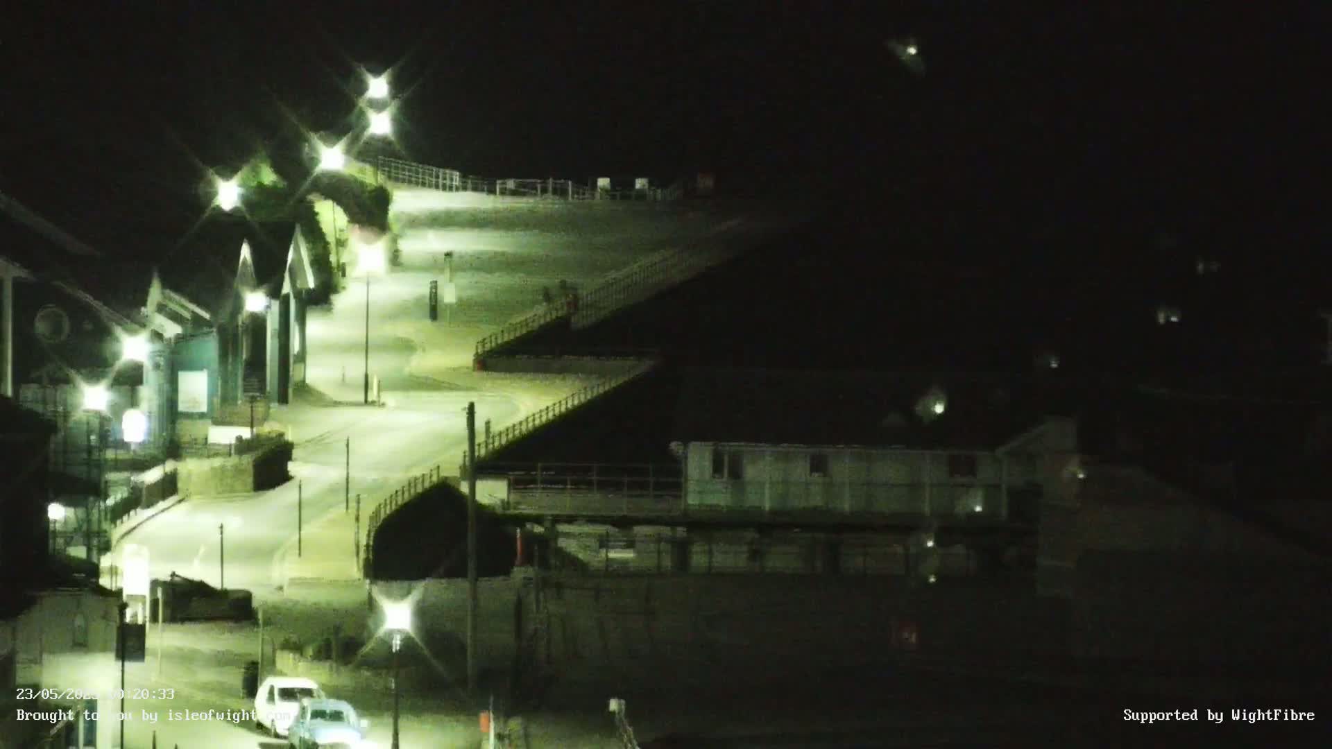 A nighttime, illuminated view of a sloped roadway and buildings, possibly a harbor area.