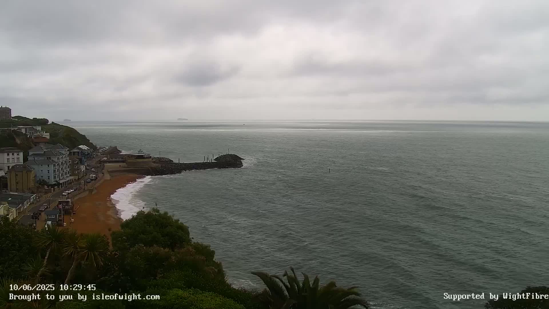 A coastal town overlooks a grey, overcast ocean with small waves lapping a sandy beach.