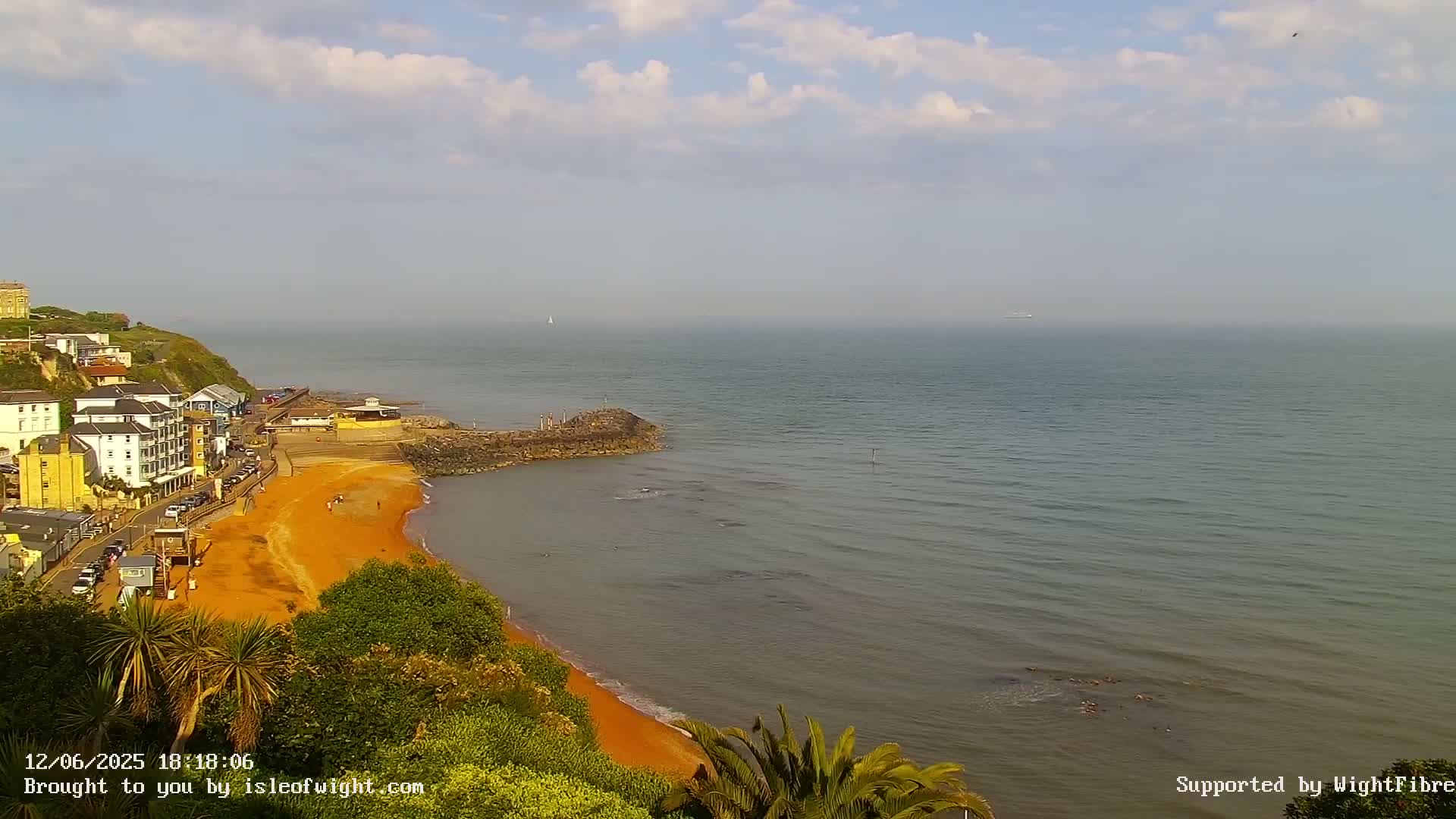 A coastal town overlooks a calm sea with a sandy beach under a partly cloudy sky.
