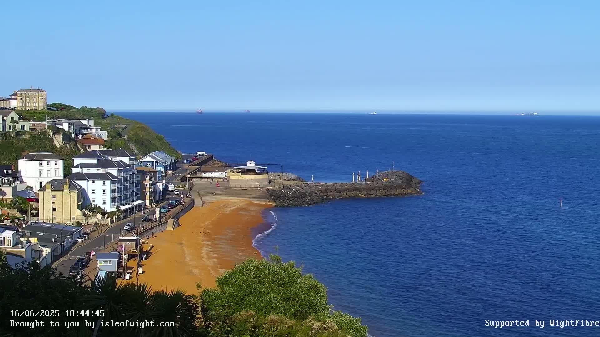A coastal town overlooks a sandy beach and calm blue ocean under a clear sunny sky.