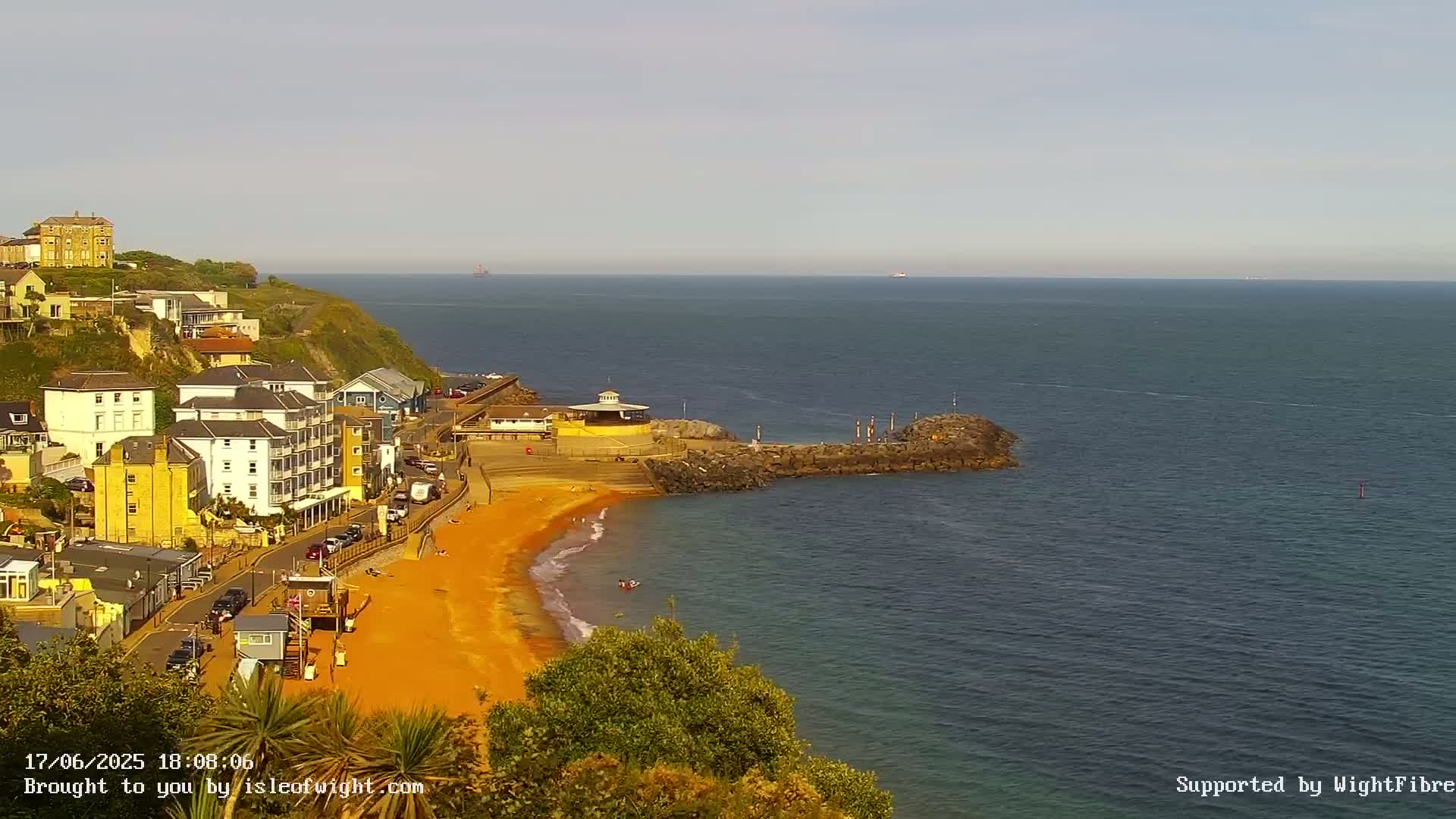 A seaside town with colorful buildings on a cliff overlooking a calm ocean with a sandy beach below.