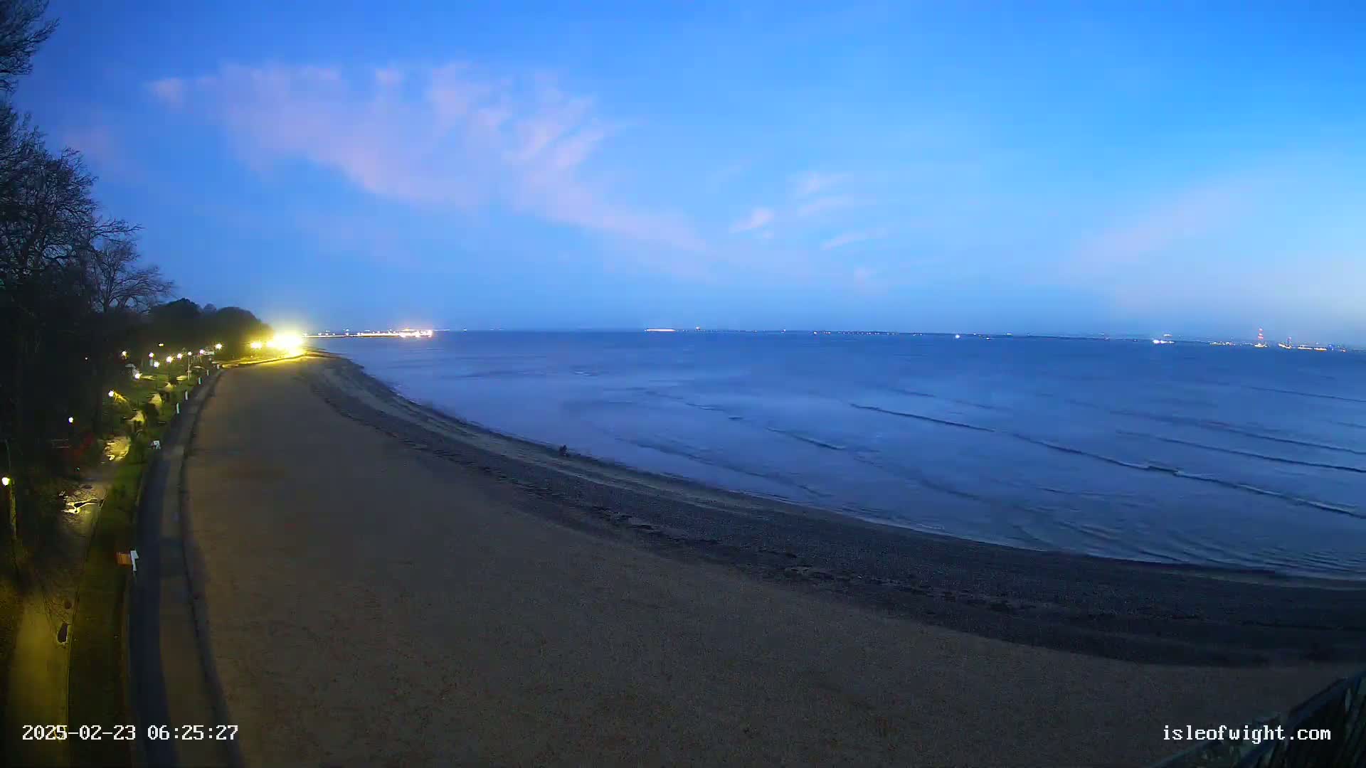 A dark sandy beach curves gently to meet a calm, dark-blue sea under a twilight sky with faint clouds.