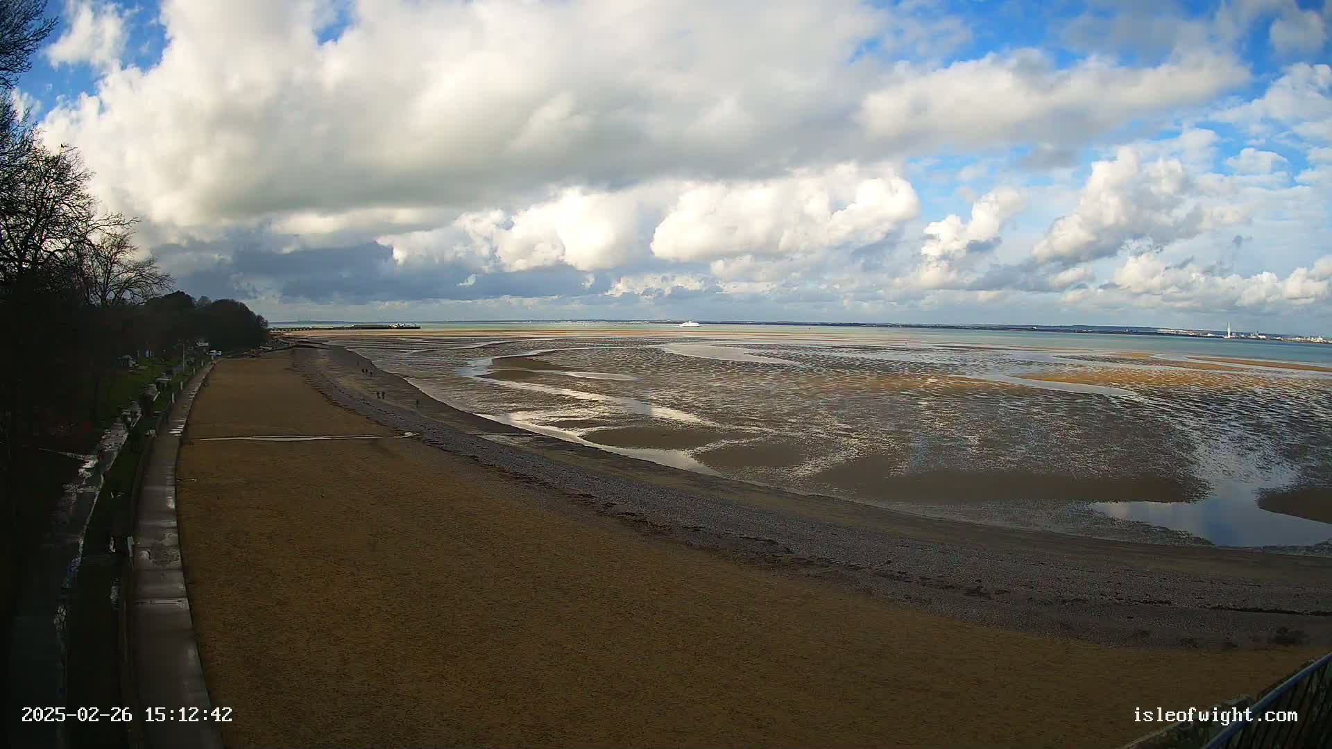 A sandy beach curves toward a wide expanse of exposed mudflats under a partly cloudy sky.
