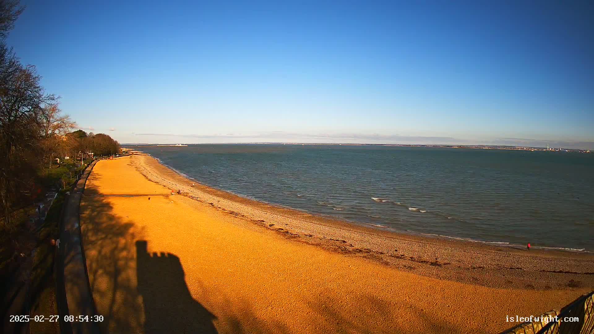 A long sandy beach curves along a calm sea under a clear blue sky.