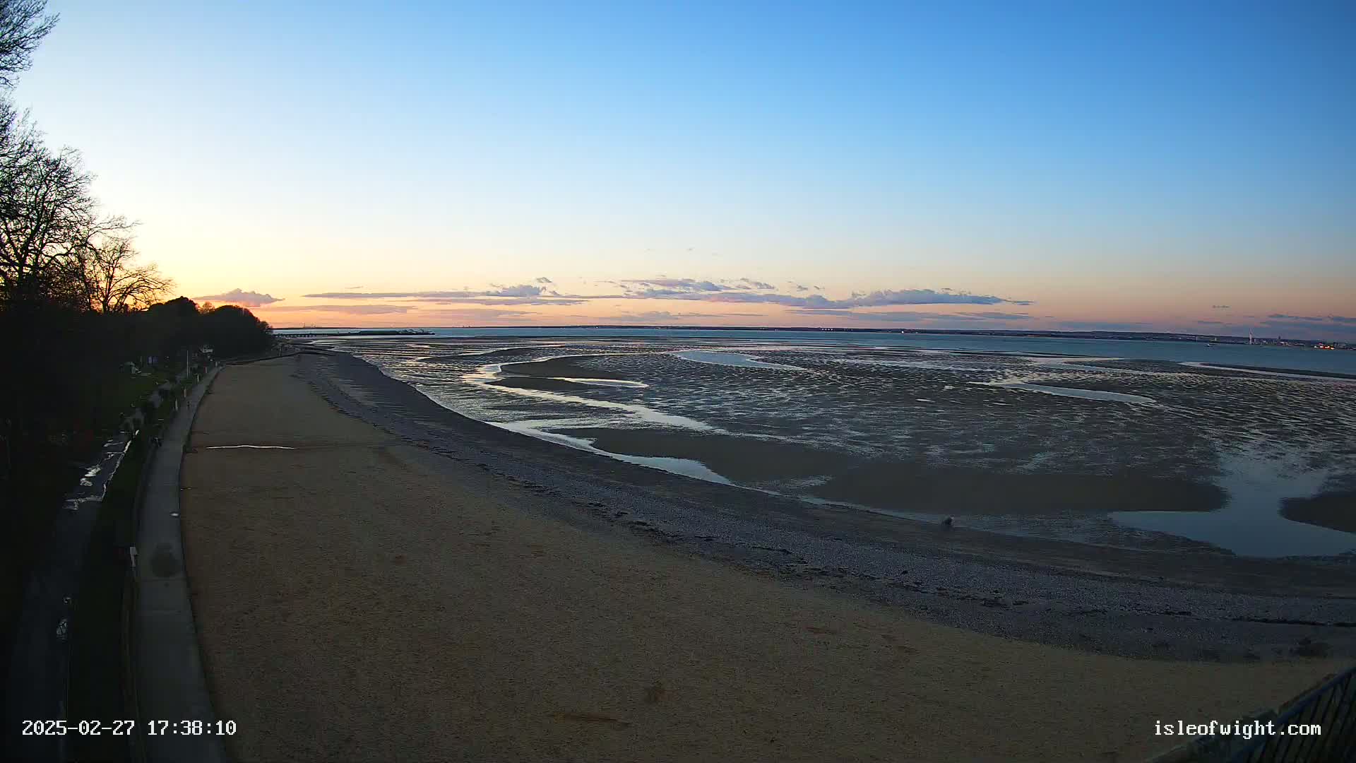 A sandy beach and a wide expanse of exposed mudflats at low tide are visible under a clear twilight sky.