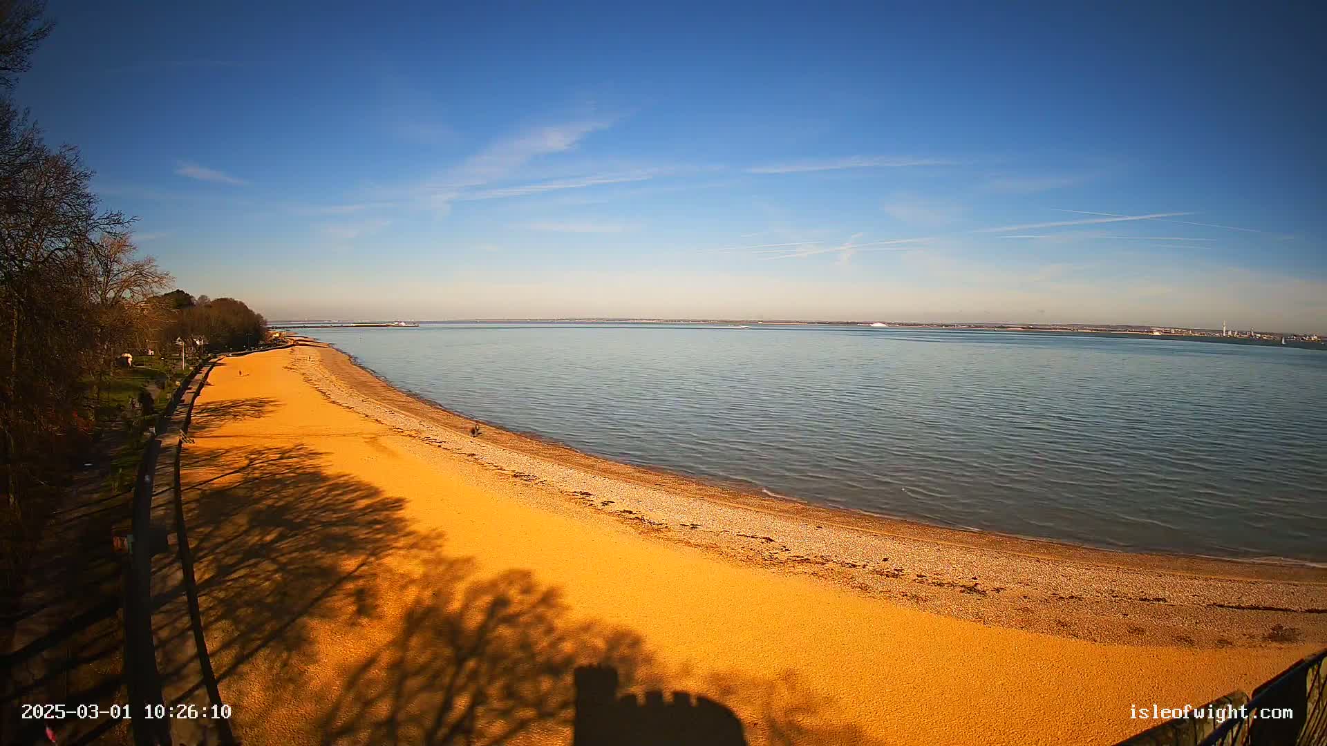 A long sandy beach curves along a calm body of water under a clear blue sky.
