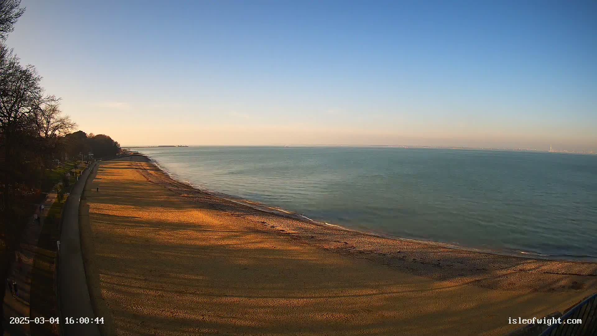 A sandy beach stretches along a calm, teal sea under a clear, bright blue sky.