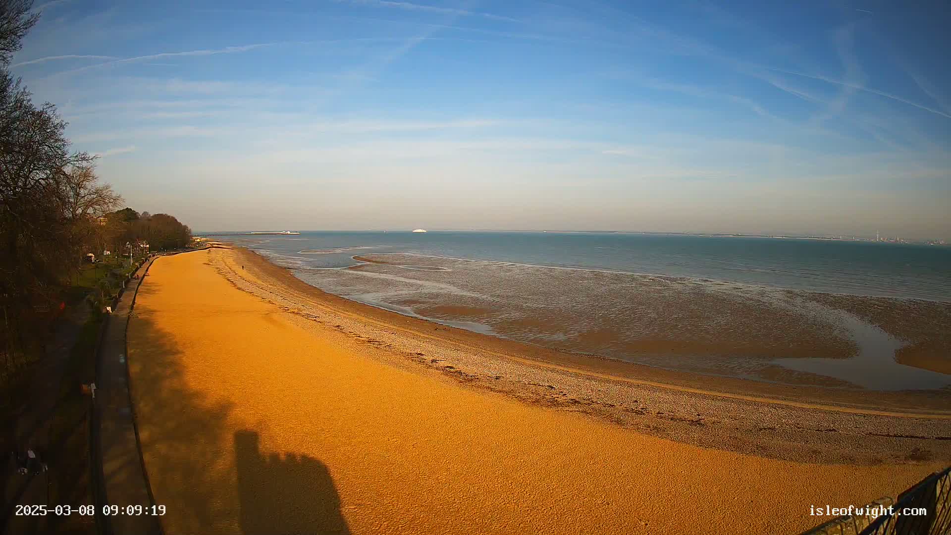 A long, sandy beach stretches along a calm, blue sea under a clear, sunny sky.