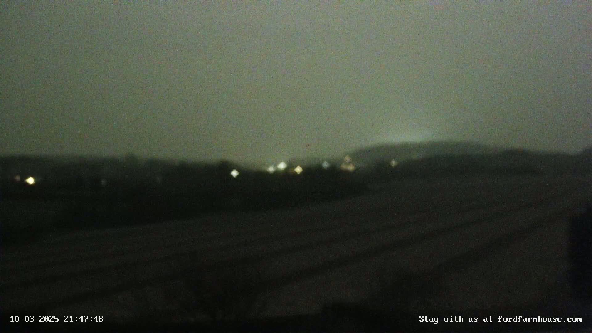 A blurry nighttime view of a dark landscape with a few distant lights under a hazy sky.