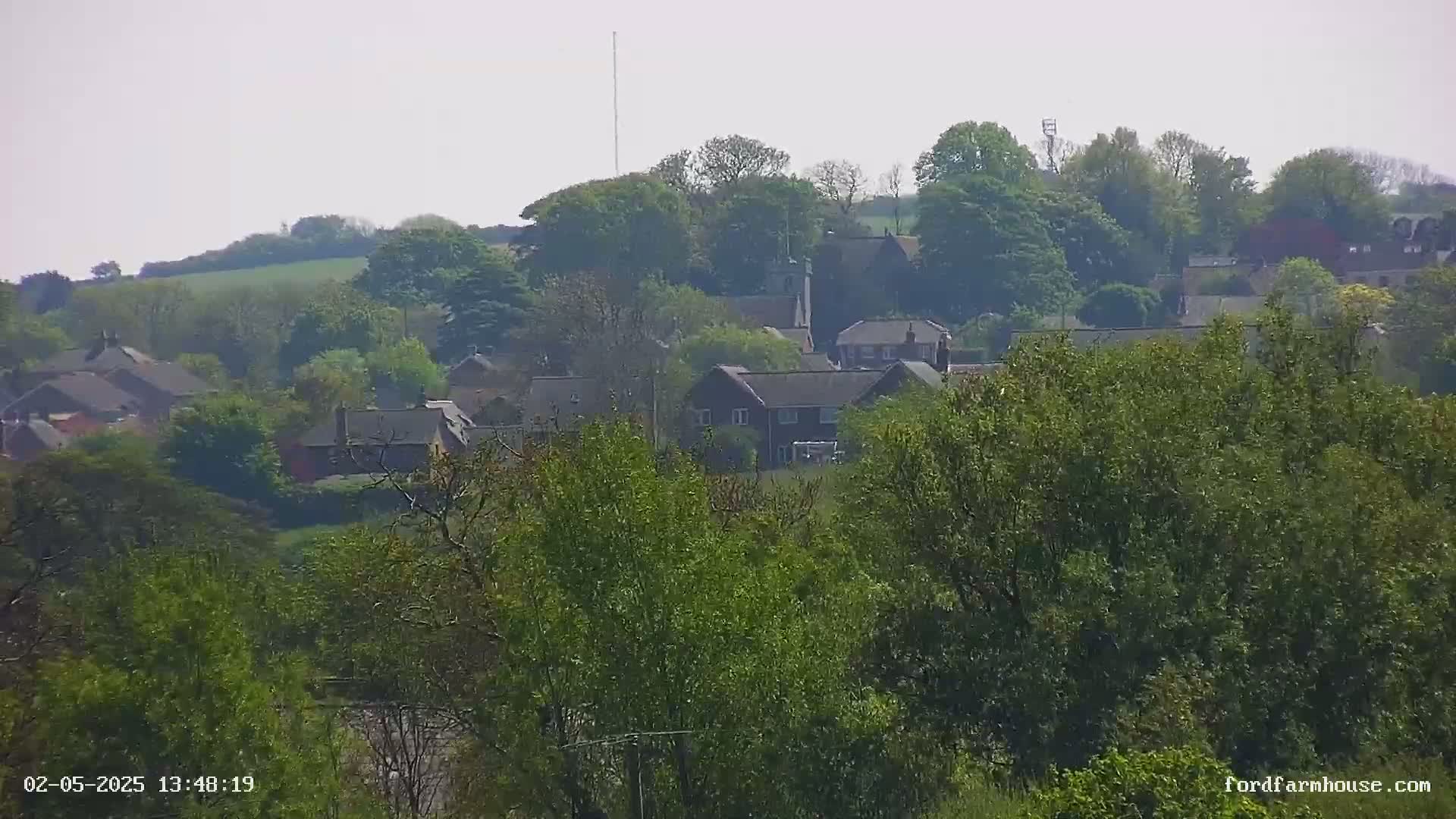 A hazy, sunny day reveals a collection of houses nestled amongst lush green trees and rolling hills.