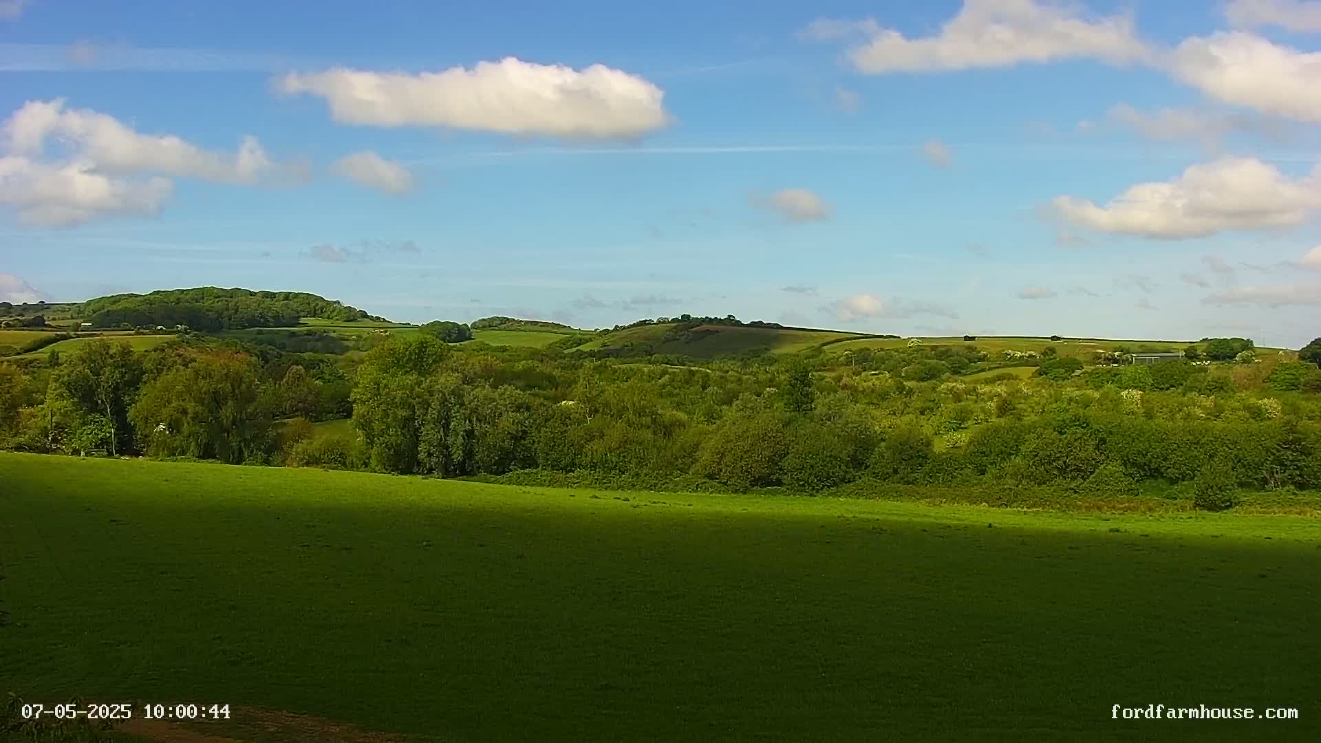 A sunny day reveals rolling green hills and lush vegetation under a partly cloudy sky.
