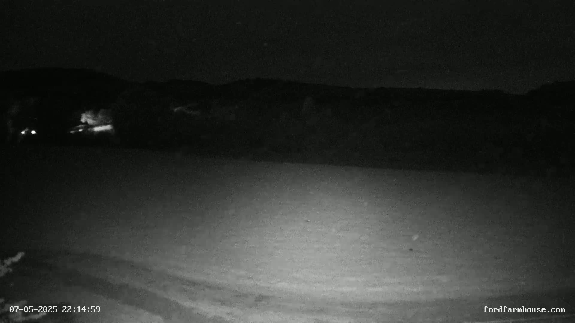 A nighttime, low-light view shows a dark, flat expanse of land with a distant, dark mountain range under a clear sky.