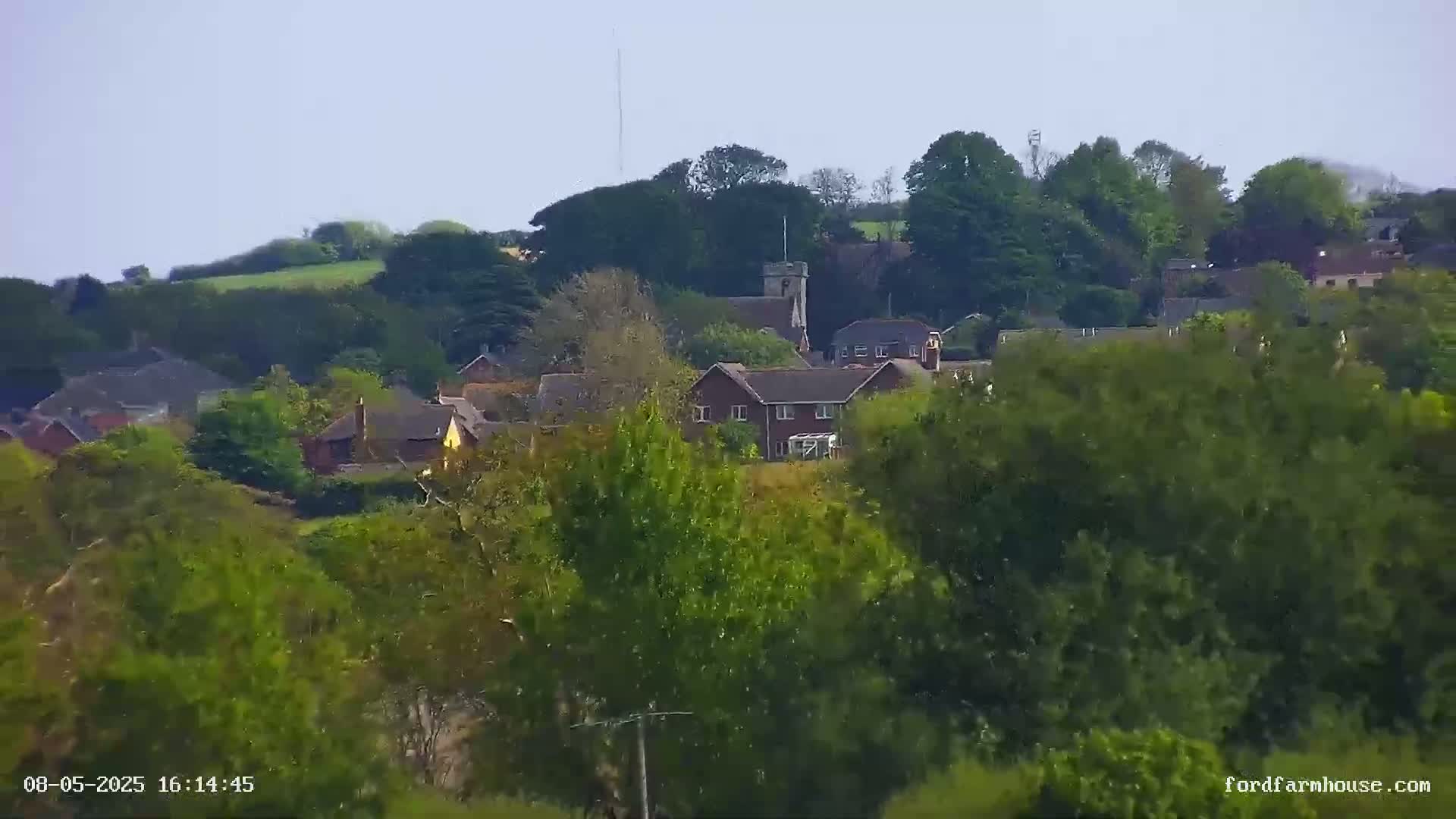 A distant view of a village nestled among green hills and trees under a clear sky.