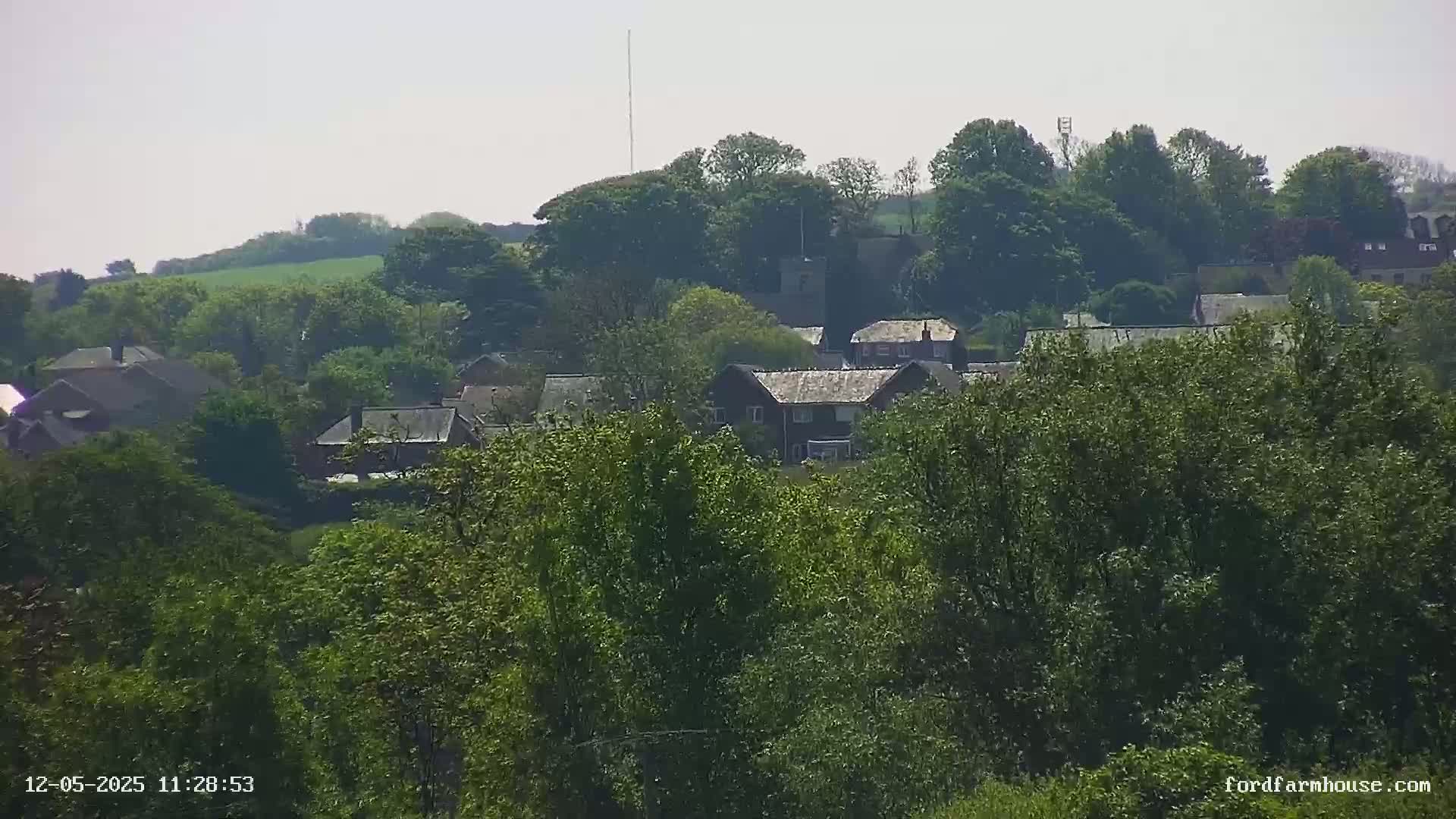 A distant view of a village nestled amongst lush green trees and fields under a hazy sky.