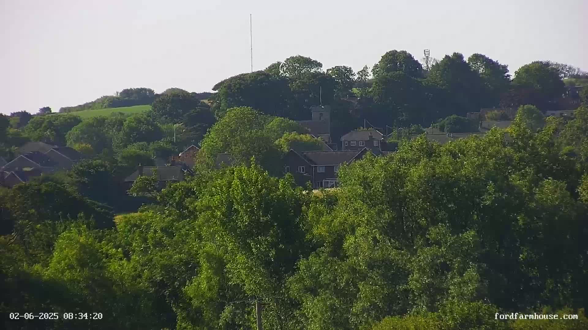 A view of a small town nestled among lush green trees and hills on a sunny day.