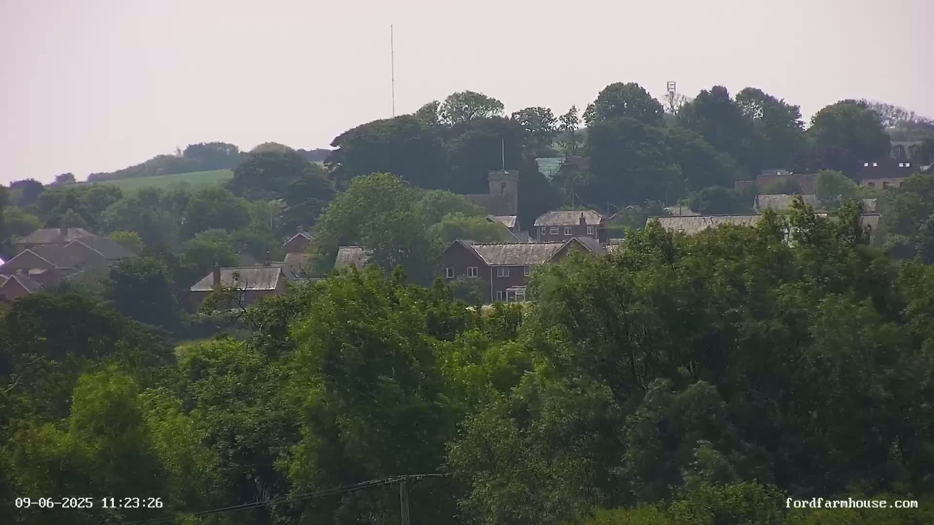 A distant view of a small village nestled among lush green trees on a hazy day.