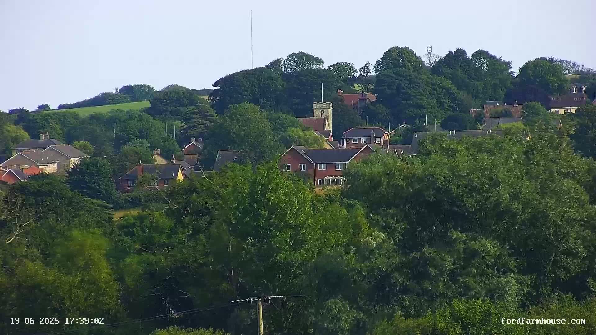 A small village nestled among lush green trees on a hill under a clear sky.