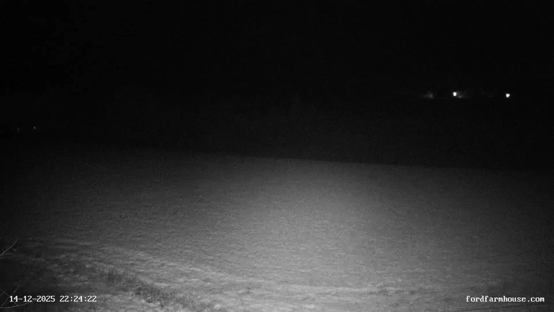 An overcast and cool morning reveals a rural landscape with several houses and outbuildings nestled among rolling green pastures and tilled fields, bordered by trees displaying late autumn foliage, and a red vehicle visible near a fenced track.